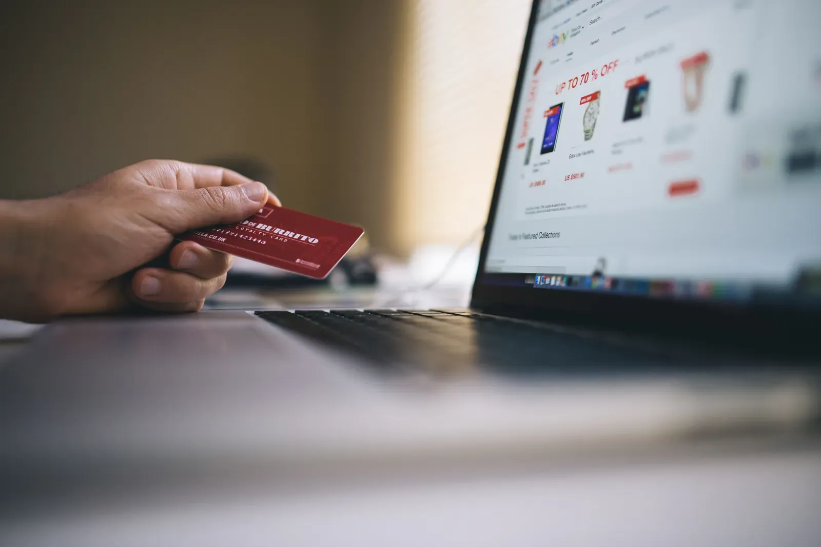 Mano con una tarjeta frente a una laptop con una tienda en línea abierta